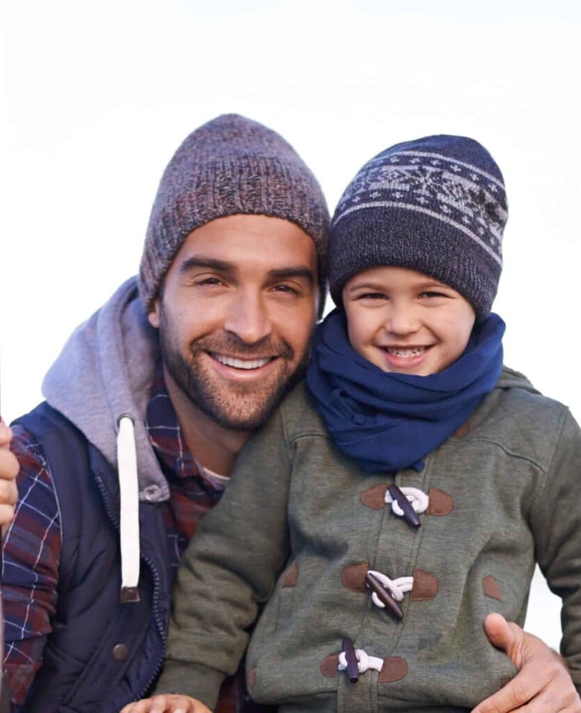 Smiling father and young boy wearing winter hats during fishing trip